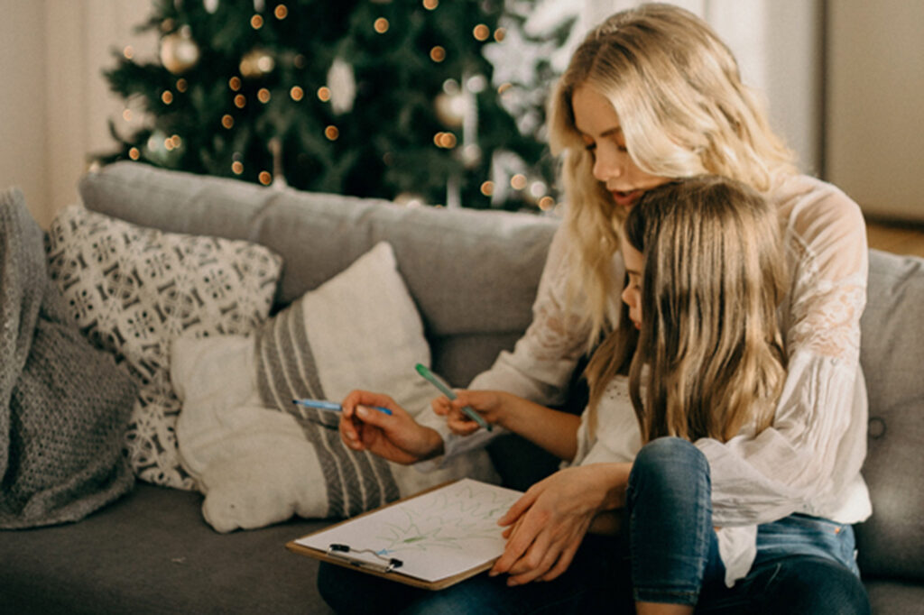 Mother and daughter creating a Christmas card sitting on the sofa.